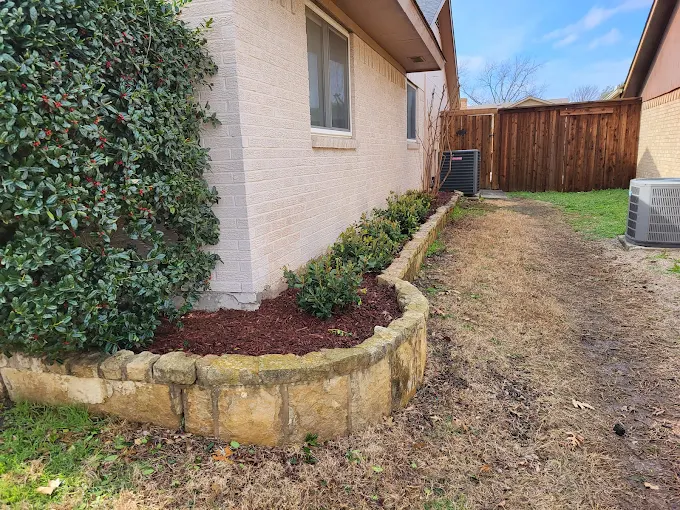 Curved stone retaining wall with shrubs in a side yard